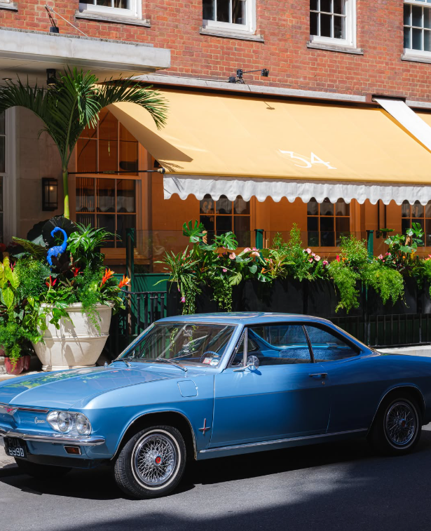 The honey-yellow awning of 34 Mayfair in morning light, a vintage car parked outside