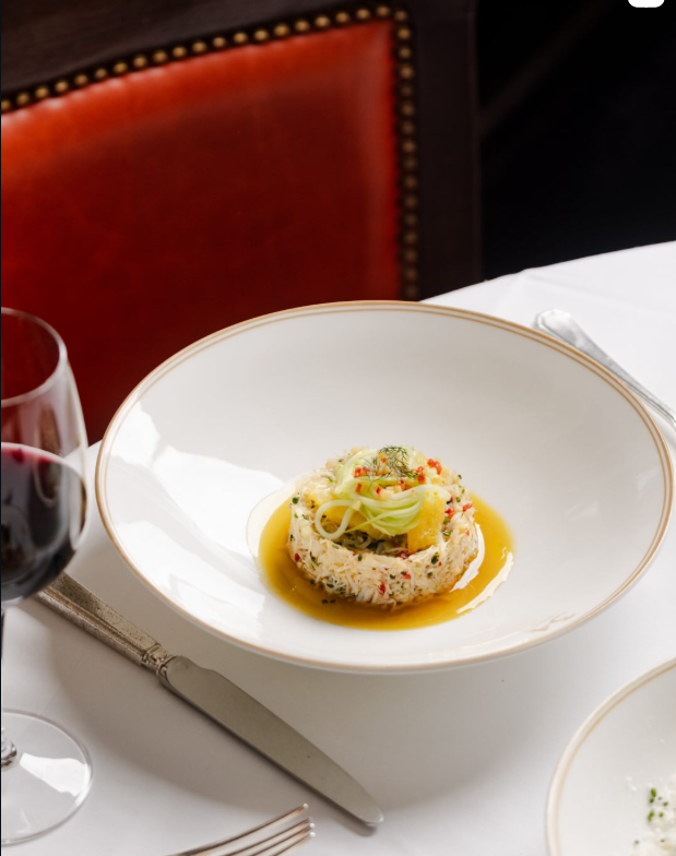 Dorset crab tartare on gold-rimmed china against an oxblood leather banquette