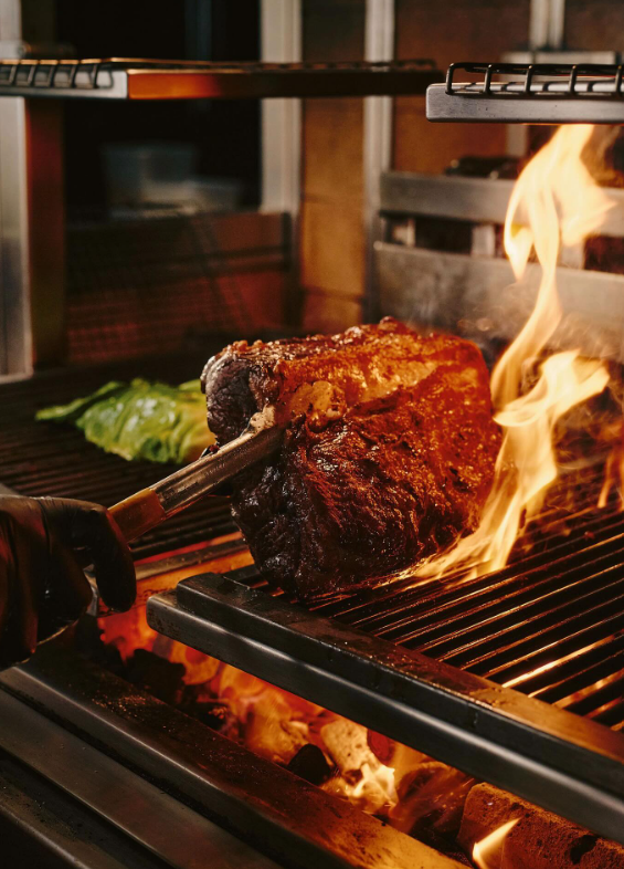 A rib of beef held over open flame on the charcoal grill